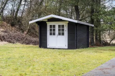 a black shed with a white door in a yard at LF10307-Hurup-Thy-Traelobervej-7 in Sønder Ydby