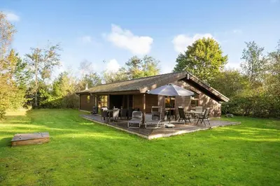 a log cabin with chairs and an umbrella in the grass at JB245-Fjerritslev-Tyttebaerstien-44 in Fjerritslev