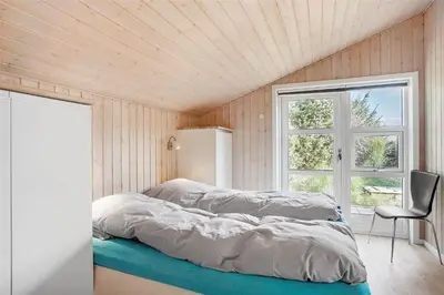 a bedroom with a bed with a chair and a window at JB133-Fjerritslev-Blabaerstien-35 in Fjerritslev