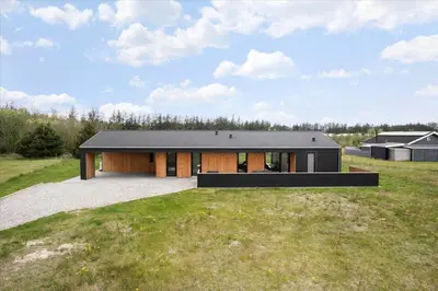 a house with a black roof on a grass field at JB141-Brovst-Kronvildtvej-86 in Brovst
