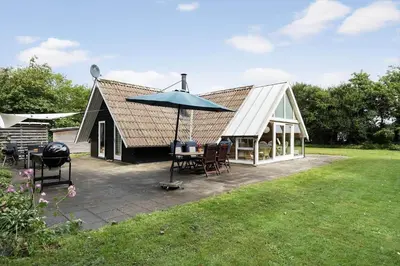 a house with a table and an umbrella on a patio at 80179-Vemb-Harpotvej-74 in Vemb
