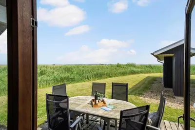 a table and chairs on a porch with a view of a field at 70721-Ulfborg-Klitengene-11 in Ulfborg