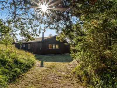 a log cabin with the sun shining through the trees at Holiday Home Anneka - 750m from the sea by Interhome in Pandrup