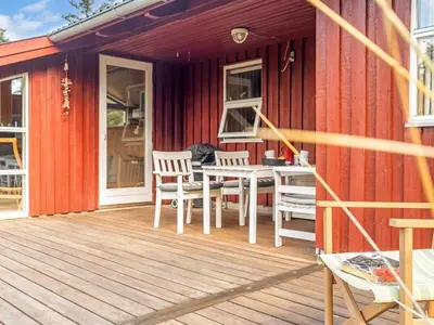 a red house with a deck with a table and chairs at Holiday Home Ingobert - 600m from the sea by Interhome in Saltum