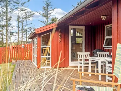 a red tiny house with a deck and chairs at Holiday Home Ingobert - 600m from the sea by Interhome in Saltum