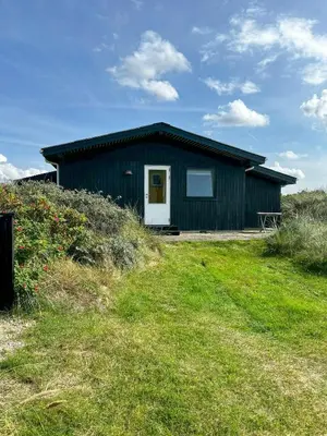 a black house with a white door on a grass field at Family House Close To The Sea At Tranum Strand in Brovst