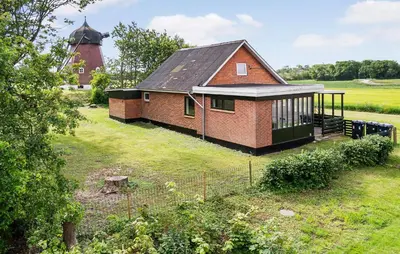 a small brick house in a field with a windmill at 1 Bedroom Nice Home In Hurup Thy in Ullerup
