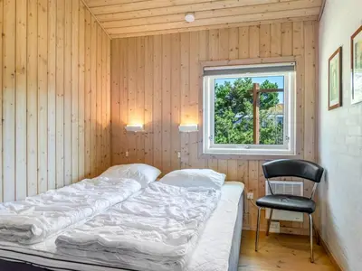 a bed in a room with a window and a chair at Holiday Home Melita - 2km from the sea by Interhome in Blokhus