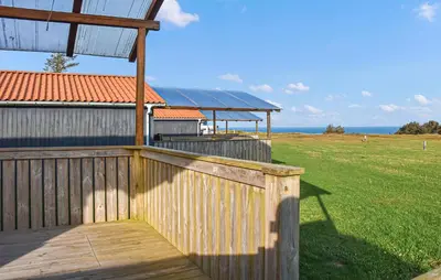a wooden fence and a building with a field and the ocean at Lovely Home In Hanstholm With Private Swimming Pool, Can Be Inside Or Outside in Hanstholm