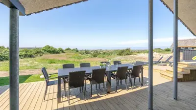 a dining table and chairs on a deck with the beach at Villavilla 909 - Blokhus, Nordjylland in Blokhus