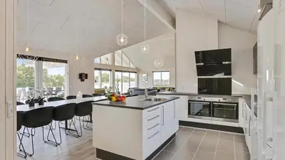 a kitchen with white cabinets and a bar with black chairs at Villavilla 405 - Hostrup Strand, Limfjorden in Spottrup