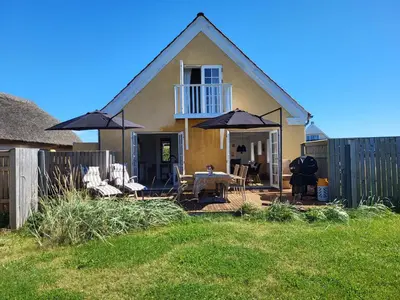 a house with a table and chairs and an umbrella at Strandhuset in Agger