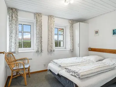 a bedroom with a bed and a chair and windows at Holiday Home Siljana - 200m from the sea by Interhome in Lemvig