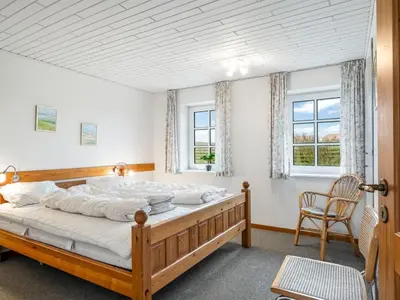 a bedroom with a wooden bed and two windows at Holiday Home Siljana - 200m from the sea by Interhome in Lemvig