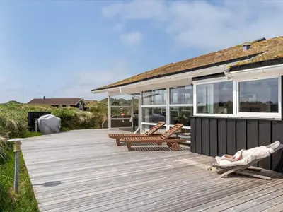 a wooden deck with two chairs and a house at Holiday Home Osfrid - 175m from the sea by Interhome in Blokhus