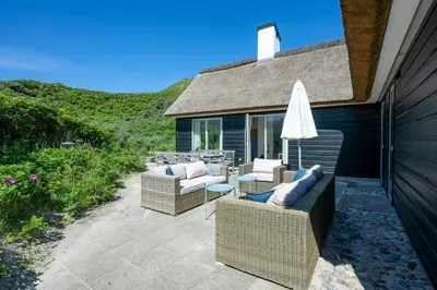 a patio with two chairs and an umbrella at Thatched House At First Dune Row In Blokhus in Blokhus