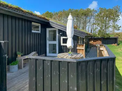 an outdoor deck with an umbrella and a table and chairs at Holiday Home By The North Sea Dunes In Rødhus in Pandrup