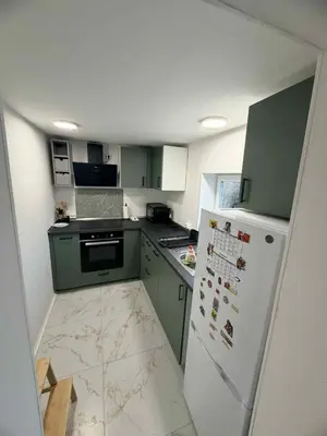 a small kitchen with green cabinets and a white refrigerator at Hel hus i rolig by in Birkelse