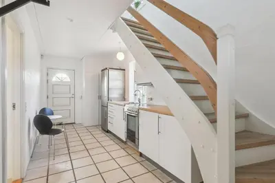a kitchen with white cabinets and a wooden stairway at Holstvej 21 in Blokhus