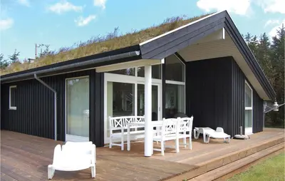 a black house with white chairs on a wooden deck at Holiday Home Pandrup 07 in Pandrup