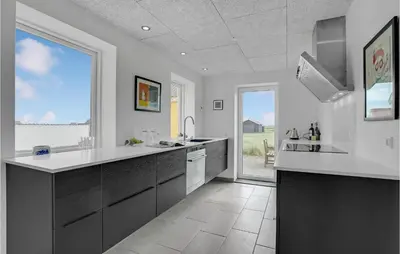 a kitchen with white and black cabinets and a large window at Klitrosen in Harboør