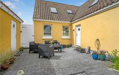a patio with furniture and a yellow house at Klitrosen in Harboør