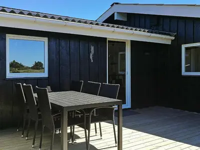 a dining table and chairs on a deck with a house at 9 person holiday home in Løkken-By Traum in Grønhøj
