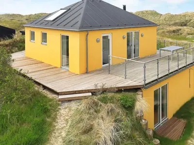 a yellow house with a wooden deck on a hill at Luxury Seaside Retreat - By Traum Ferienwohnungen in Tranum Strand