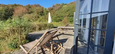 a deck with two chairs and a table and an umbrella at Næsbydale Badehotel in Ranum