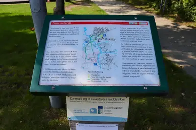 a sign in the grass next to a sidewalk at Plexus Hytterne in Holstebro