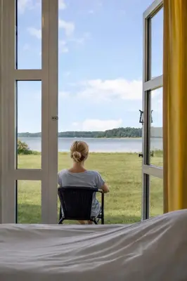 a woman sitting in a chair looking out of a window at Hotel Pinenhus in Glyngøre
