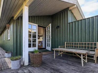 a green building with a bench on a deck at 6 person holiday home in Løkken-By Traum in Løkken