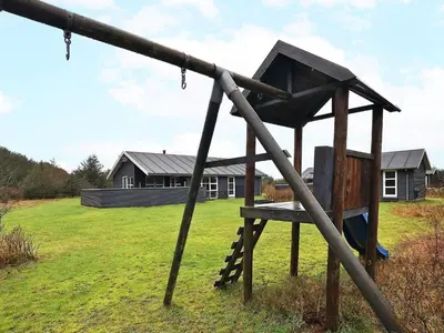 a wooden swing set in a field with a house at Modern Retreat with Spa - By Traum Ferienwohnungen in Løkken