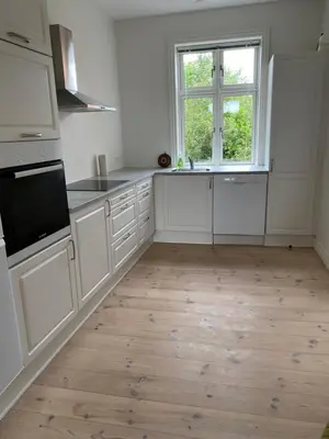 a kitchen with white cabinets and a wooden floor at Strømpehuset in Øster Assels
