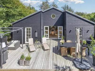 a black house with a wooden deck with chairs at 6 person holiday home in Blokhus-By Traum in Blokhus