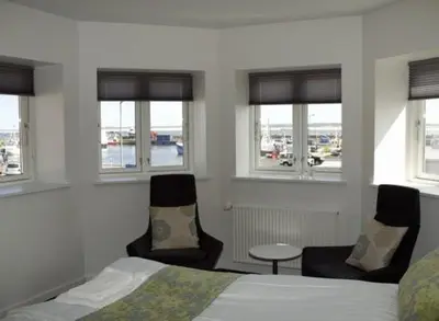 a bedroom with a bed and two chairs and windows at Seaside Hotel Thyborøn in Thyborøn