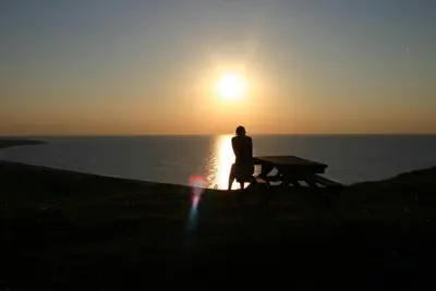 a person sitting on a picnic table watching the sunset at Hotel Højgaarden in Slettestrand