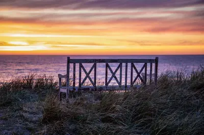 a bench sitting on the beach at sunset at Bredgade 10 Thyborøn in Thyborøn