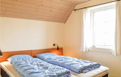a bed with blue sheets in a room with a window at Nice Home In Harboøre With Kitchen in Harboør