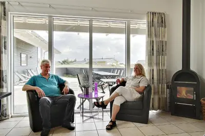 two people sitting in chairs in a living room with a fireplace at Luksus-poolhus B5 in Harboør