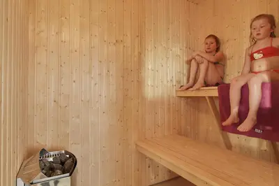 two children sitting on shelves in a sauna at Luksus-poolhus L21 in Harboør