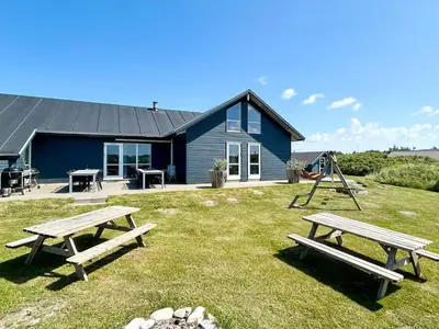 two picnic tables in front of a blue house at 18 person holiday home in Harboøre in Harboør