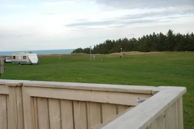 a rv parked in a field next to a fence at Hytteby – Hanstholm Camping – Thy Feriepark in Hanstholm