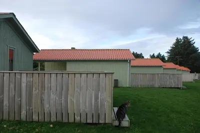 a black cat sitting on a block next to a fence at Hytteby – Hanstholm Camping – Thy Feriepark in Hanstholm