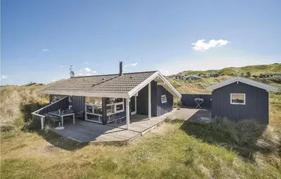 a black house with a wooden deck in a field at Beautiful Home In Blokhus With Wifi in Blokhus