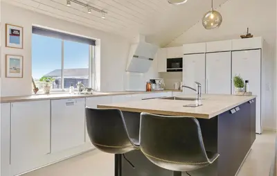 a kitchen with white cabinets and a island with chairs at 8 Bedroom Awesome Home In Thisted in Thisted
