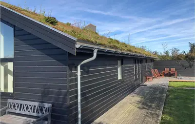 a building with a grass roof with a bench on a deck at Beautiful Home In Blokhus With Kitchen in Blokhus