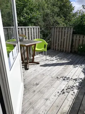 a wooden deck with a table and a green chair at Hunetorpvej Holiday Apartment in Blokhus