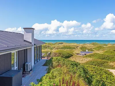 a house with a deck with the ocean in the background at 6 person holiday home in Løkken in Løkken