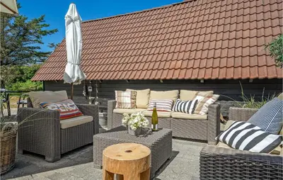 a patio with wicker chairs and an umbrella and a table at 4 Bedroom Gorgeous Home In Blokhus in Blokhus